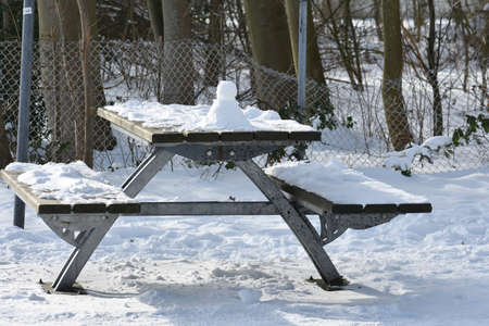 Snowy winter landscape with wooden table and benches, in the park.の写真素材