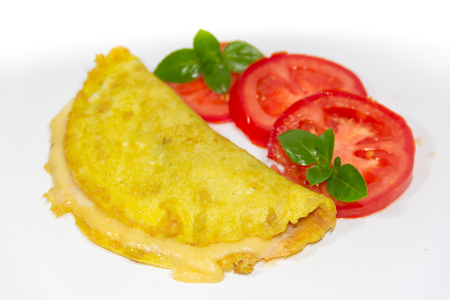 omelette made with beaten eggs stuffed with onion cheese and tomatoes on white background with sliced tomatoes and basilの写真素材