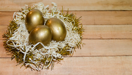 Golden easter eggs in straw nest with rustic wooden background