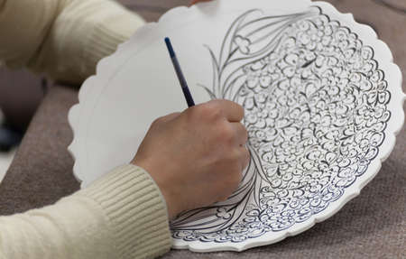 artisan drawing a flower pattern on blank plateの写真素材