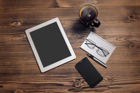 tablet computer smart phone coffee cup notepad and eye glasses on wood tableの写真素材