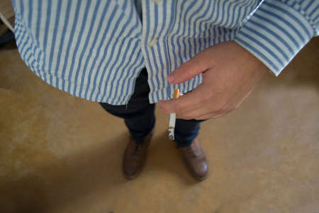 Man with brown boots and blue shirt holding a lit cigarette on his handsの写真素材