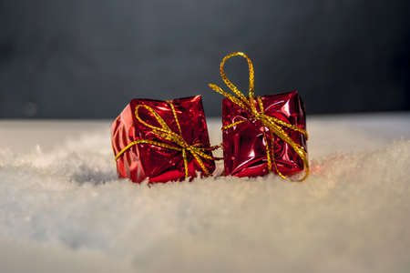 Red gift box with a golden ribbon in top of snow for christmas decoration or to put under the treeの写真素材