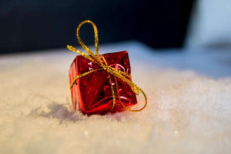 Beautiful red gift box with a golden ribbon in top of snow for christmas decoration or to put under the treeの写真素材