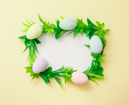 Frame with green leaves and easter eggs with white copy space on a light yellow background.の写真素材