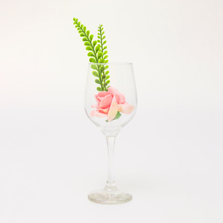 Pink rose flower and leaves on a wine glass on a white background.の写真素材