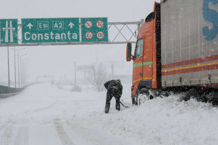 Highway A2, Romania, 17 January 2016: A truck driver shovels snow to free his truck on the closed highway A2, the main commercial route which connects Bucharest to the Black Sea's port, Constanta.のeditorial素材