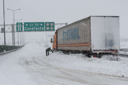 Highway A2, Romania, 17 January 2016: A truck driver shovels snow to free his truck on the closed highway A2, the main commercial route which connects Bucharest to the Black Sea's port, Constanta.のeditorial素材