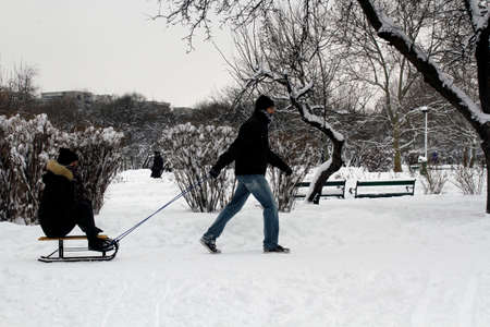 BUCHAREST, ROMANIA - January 07, 2017: A man pulls a sledge a young woman in a frozen park in the first day of winter with snow.のeditorial素材