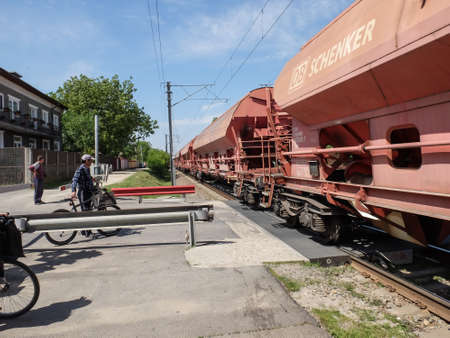 FUNDENI, ROMANIA, April 23, 2016: People on bikes stopped at train crossing while a cargo train...