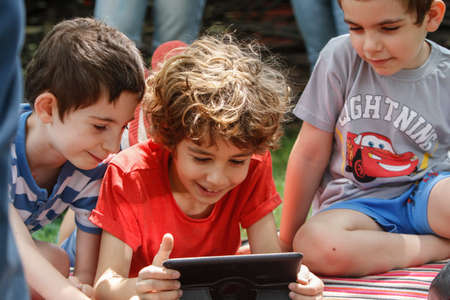 BUCHAREST, ROMANIA, June 19, 2016: Three boys play on a tablet during a fest in the Village Museum in Bucharest.のeditorial素材