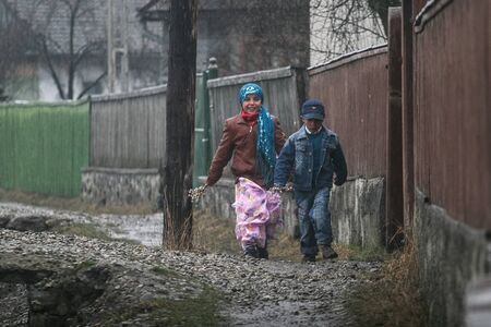 HARGHITA, ROMANIA - March 27, 2010: Gipsy kids walking near fences on a cold day.のeditorial素材