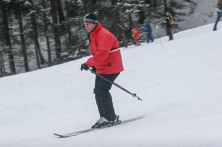 BUSTENI, ROMANIA - February 7, 2010: A men skiing down during the day wearing a red jacket.のeditorial素材