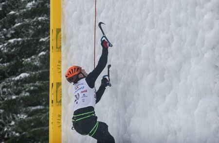 BUSTENI, ROMANIA - February 7, 2010: A man with special equipment and ice tools climbing a large wall of ice.のeditorial素材