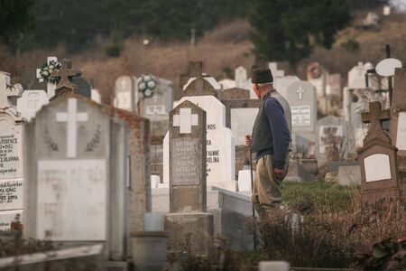 HARGHITA, ROMANIA - March 27, 2010: An older man walks between old crypts on a cemetery.のeditorial素材