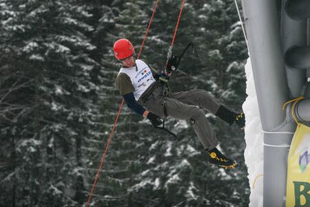 BUSTENI, ROMANIA - February 7, 2010: A man with red helmet and ice tools climbing a large wall of ice.のeditorial素材