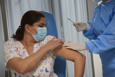 BUCHAREST, ROMANIA - Dec. 27, 2020: A member of medical personnel receives the covid vaccine during the first day of European Vaccination Campaign.のeditorial素材