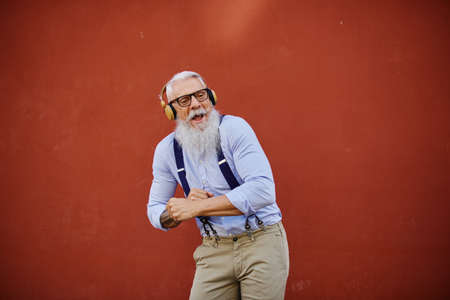 Cheerful elderly man dancing while listening to music from headsetの写真素材