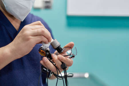 Crop anonymous ophthalmologist in respiratory mask measuring optical power of eyewear lens with...