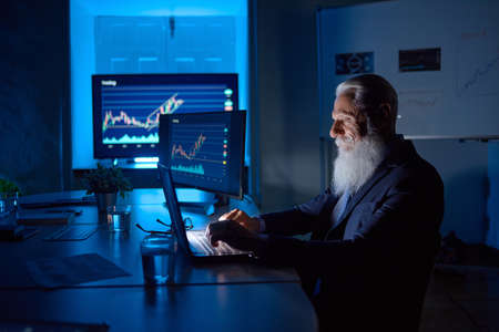 Senior employee typing on laptop in dark office