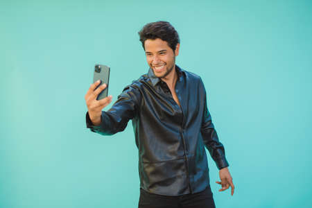 Happy man taking selfie on smartphone on aquamarine backgroundの写真素材