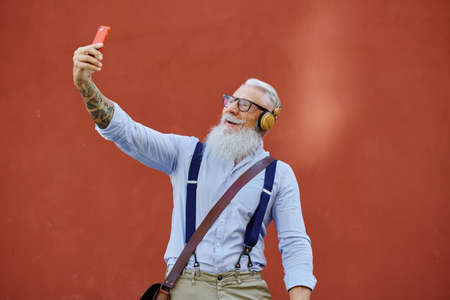 Smiling elderly man taking selfie on smartphone on red backgroundの写真素材