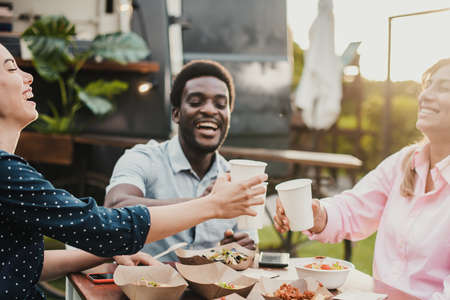Happy people eating and cheering at food truck restaurant - Focus on left girl faceの写真素材