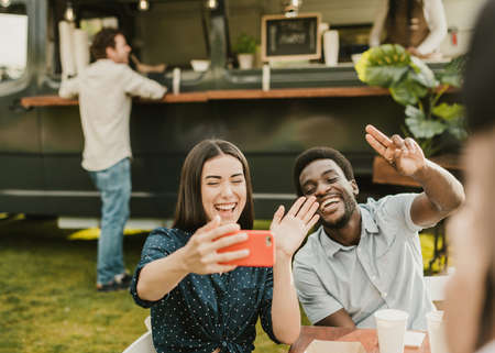 Multiracial friends having fun doing selfie eating at food truck outdoor - Focus on african man face