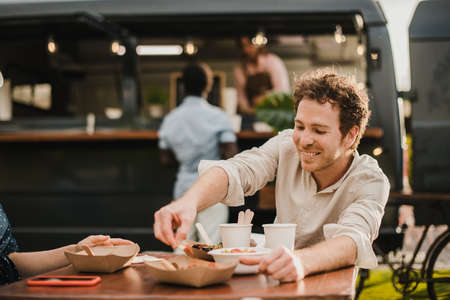 Young happy people eating at food truck outdoor - Focus on man faceの写真素材