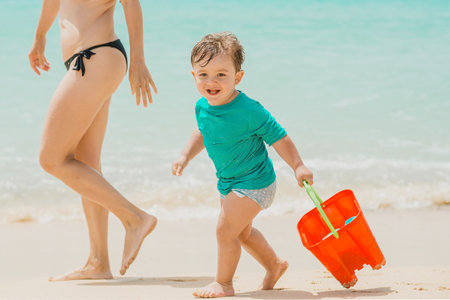 Cheerful boy with bucket having fun on beachの写真素材