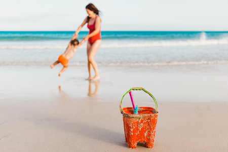 Bucket with shovels placed on beach near mother playing with sonの写真素材