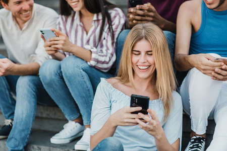 Young people having fun using mobile phones outdoor in the city - Focus on caucasian girl faceの写真素材