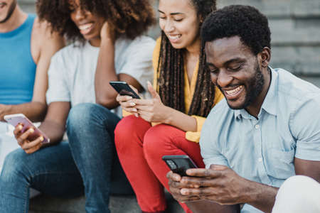 Multiracial people having fun using mobile phones outdoor in the city - Focus on african man face.