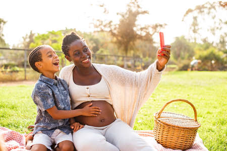 Pregnant black woman and boy taking selfie togetherの写真素材