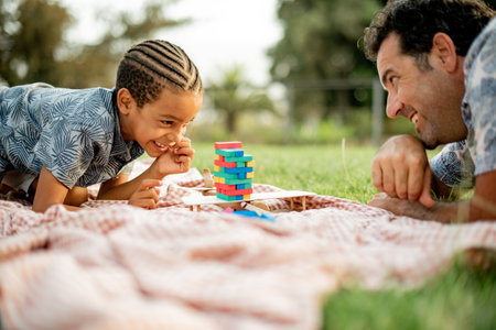 Cheerful multiethnic father and son playing block tower game in park