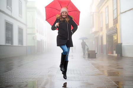 happy adult woman with jumped red umbrella on a rainy and foggy day