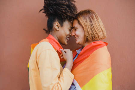 Diverse lesbian couple embracing under rainbow flagの写真素材