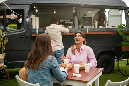 Cheerful women eating street food near truckの写真素材