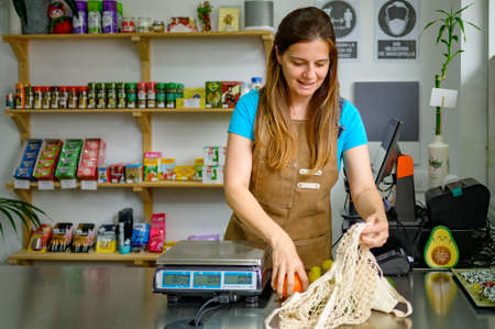Cheerful saleswoman taking out fruits near scales