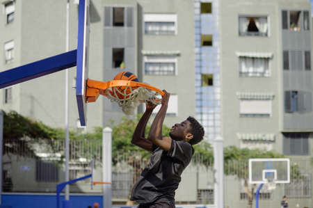 Black man performing slam dunk while playing basketballの写真素材