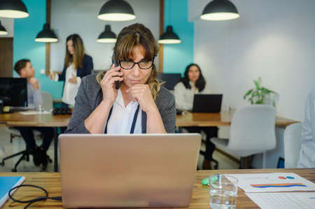 Businesswoman talking on smartphone in modern workspaceの写真素材