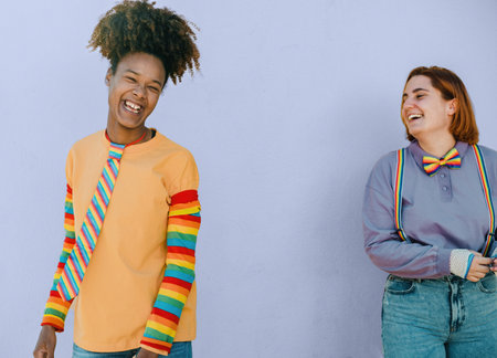 Cheerful multiethnic lesbian couple standing against blue backgroundの写真素材