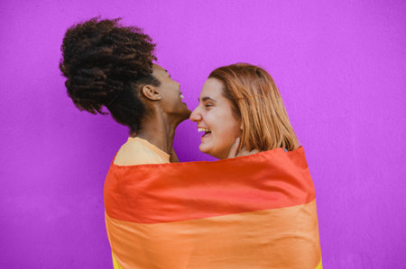 Happy multiethnic lesbian couple hugging and laughing against purple backgroundの写真素材