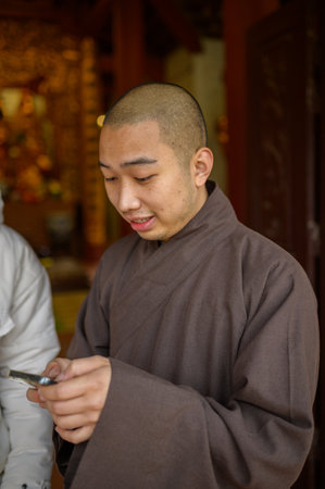Modern Asian male monk in black garment standing near temple and browsing mobile phoneの写真素材