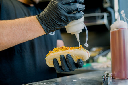 Unrecognizable street food vendor pouring sauce on hot dogの写真素材