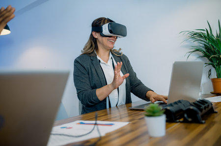 Happy female employee in VR goggles typing on laptop in officeの写真素材
