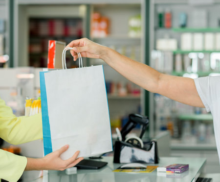 Crop pharmacist giving paper bag with pills to clientの写真素材