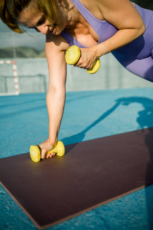 Woman doing exercises with dumbbells on sports ground