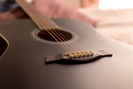 Black acoustic guitar on a bed a sunny day in a beautiful roomの写真素材