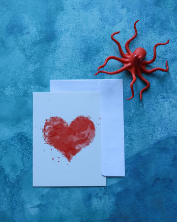 blank paper card with a heart and a toy octopus on a blue watercolor backgroundの写真素材